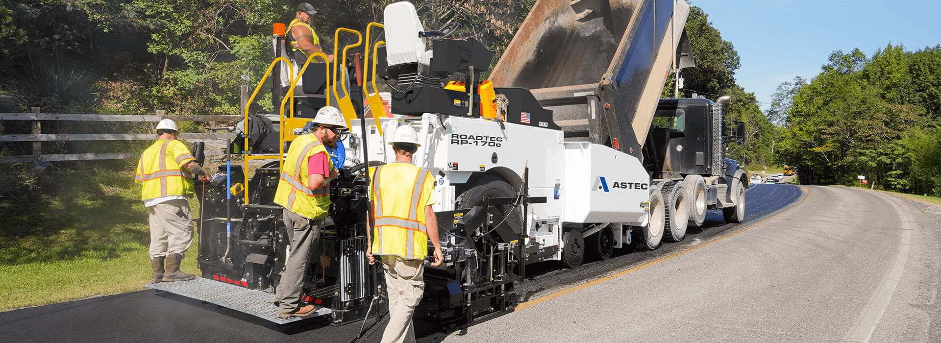 Roadtec RP-170 highway class asphalt paver paving a road with dump truck dumping into hopper
