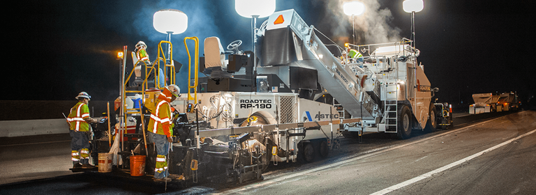 Roadtec RP-190 Highway Class Asphalt Paver paving a road at night with a Roadtec Shuttle Buggy MTV