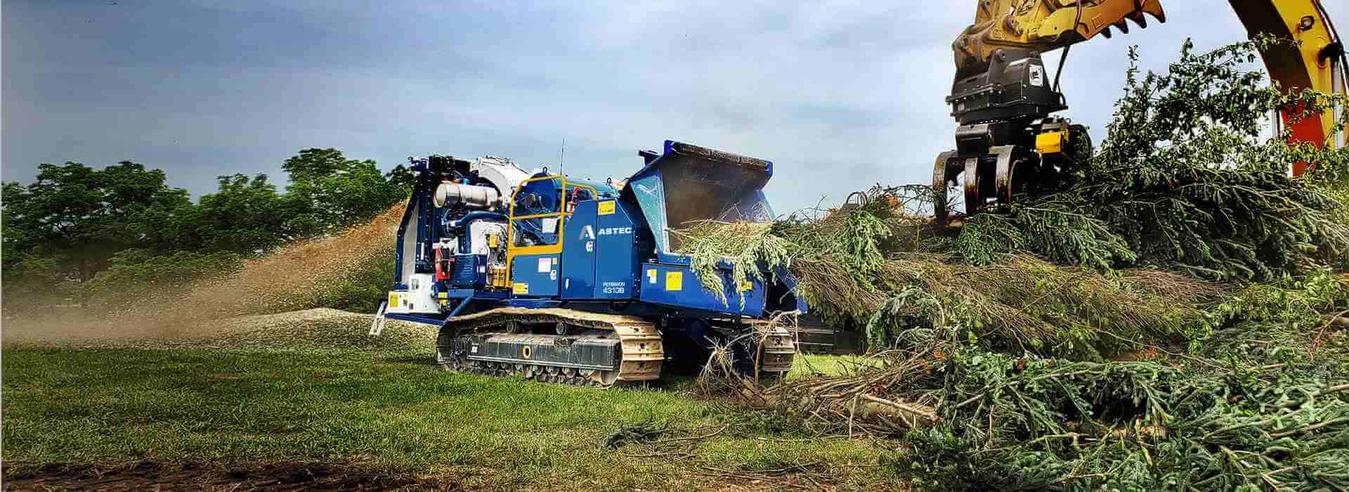 Peterson 4310B Drum Chipper chipping whole trees making microchips and being loaded by a grapple excavator