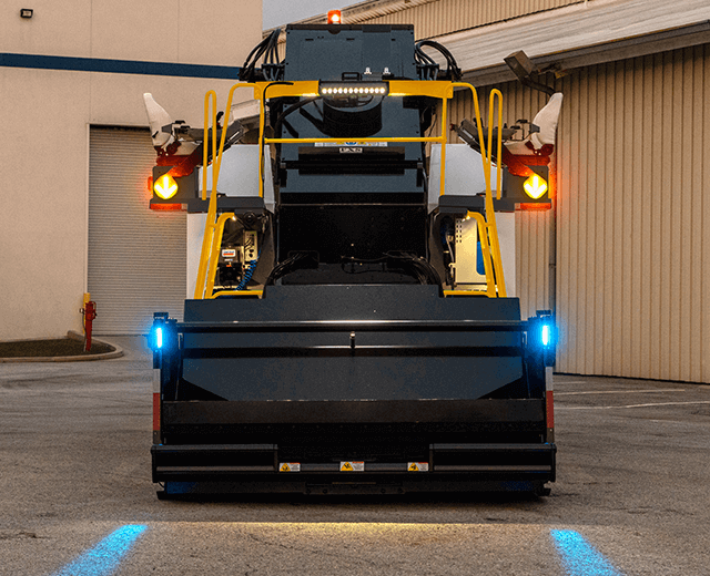 The Roadtec SB-3000 Shuttle Buggy Material Transfer Vehicle showing the front projectors that display blue lines on the ground that serve as guides for trucks