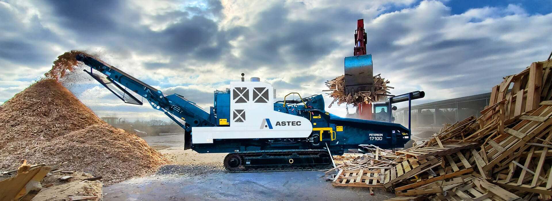 An Astec Peterson 1710D Horizontal Grinder recycling pallets into mulch and being loaded with an excavator.